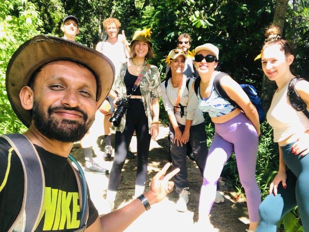Local guide Ravi leading smiling hikers wearing trail flowers through a lush Knuckles jungle trail