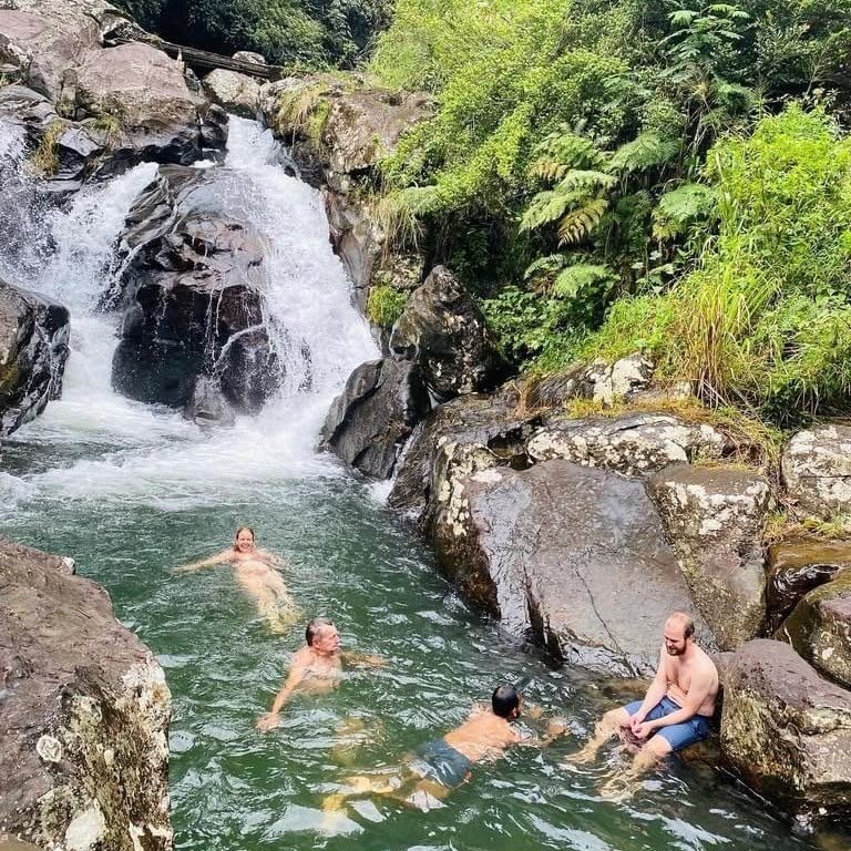 Adventure travelers swimming and relaxing in a natural cascade rock pool beneath a Knuckles waterfall
